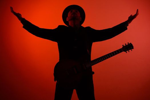 guitarist in a hat is standing with his arms outstretched