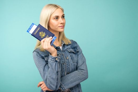 Dreamy girl in a denim jacket holds a passport with airline tickets