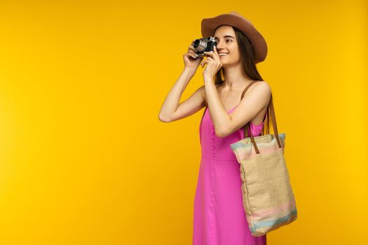 Happy girl in a pink dress and sunglasses holding camera on a yellow background