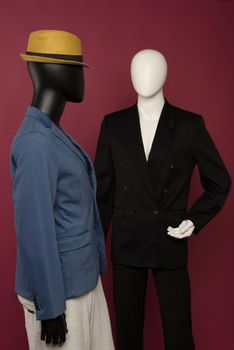 Two male mannequin in a black business suit and in a blue suit and white pants on a ruby background