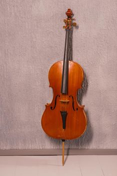 old battered cello standing near a gray textured wall