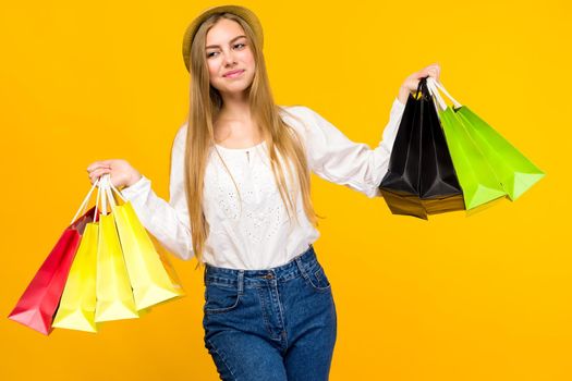 Caucasian teenage girl on yellow background. Stylish young woman with shopping bags in hands