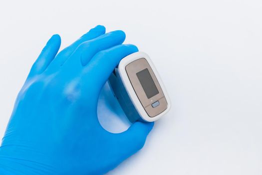 Doctor hand in protective medical gloves holding fingertip pulse oximeter on a white background, closeup