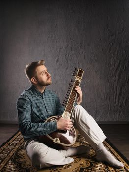 Portrait of a European man playing the sitar sitting on the carpet