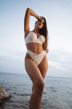 Sexy beautiful woman in white swimwear at sea coast on sunset