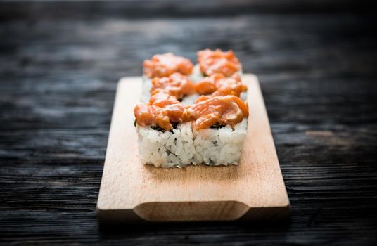 set of sushi rolls with salmon topping on wooden board