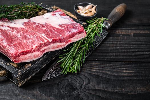 Fresh Raw veal short ribs in a wooden tray with herbs. Black wooden background. Top view. Copy space