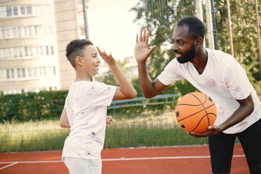 Black father with his multiracial son playing basketball in basketball court together