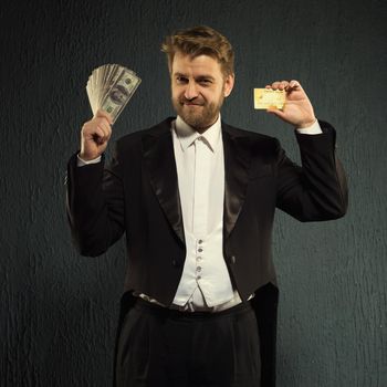Positive man in a tailcoat offers a credit card and money.