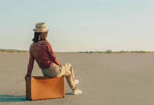 Traveler woman sitting on suitcase on road, copy-space