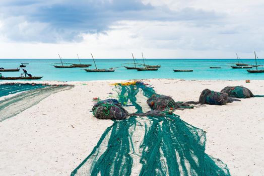 large fishing nets lying on african beach with boats near the shore