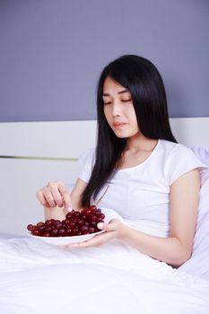 woman with red grape on bed in bedroom