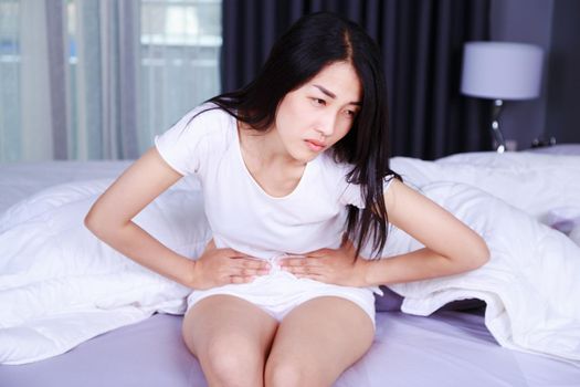 woman with stomach ache on bed in bedroom