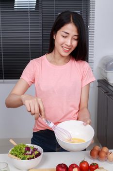 woman cooking and whisking eggs in a bowl in kitchen 