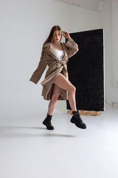 attractive caucasian skinny girl in raincoat posing on white studio cyclorama