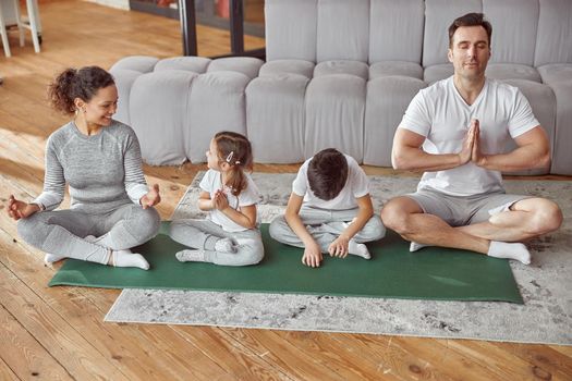 Cheerful parents teaching kids doing meditation at home