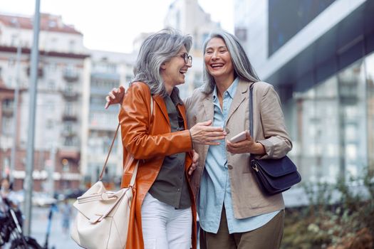 Beautiful grey haired women companions on modern city street at walking