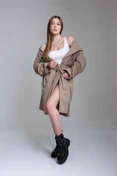 attractive caucasian skinny girl in raincoat posing on white studio cyclorama