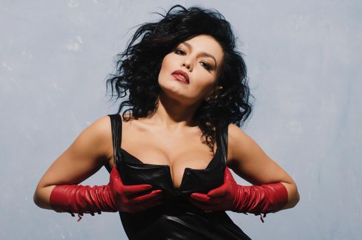 Luxurious Asian woman in black leather dress and red gloves holding his chest. Dominant Fetish Lady.