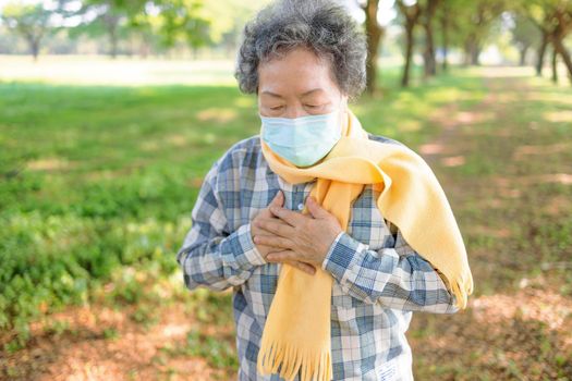 Senior woman wearing medical mask and  clutching her chest in pain