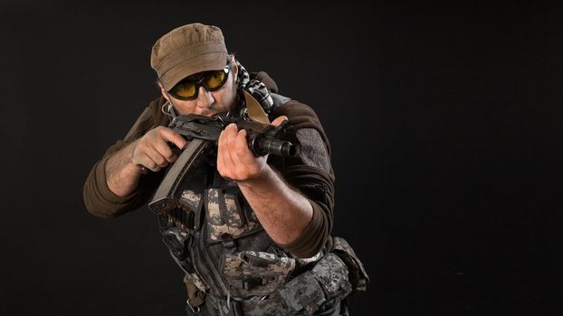 A mercenary with a gun aims at the enemy. Close-up on a dark background.