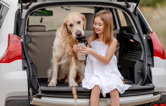 Preteen girl with golden retriever dog in car trunk