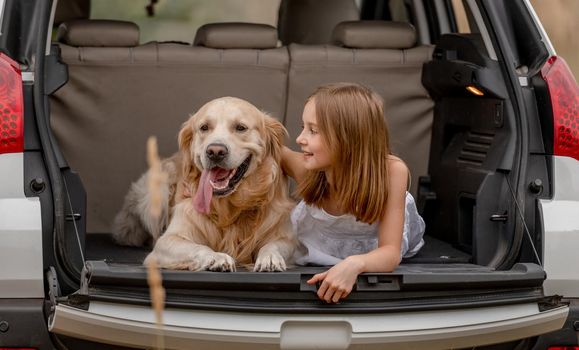 Preteen girl with golden retriever dog in car trunk