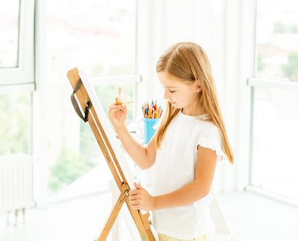 Kid girl painting different pictures on easel