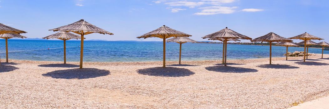 Empty Beach in Croatia. Sunshades on blue sky background on Adriatic seashore . Summer background banner.