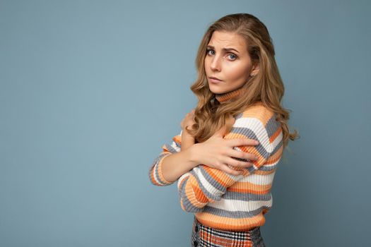 Photo shot portrait of young nice winsome beautiful sad upset sorrowful deplorable blond woman with sincere emotions wearing striped sweater isolated over blue background with free space