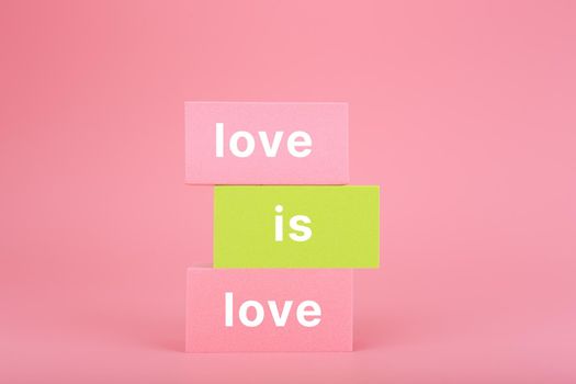 Love is love written on stack of yellow and pink rectangles on pink background. Lgbtq plus concept