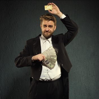 Positive man in a tailcoat offers a credit card and money.