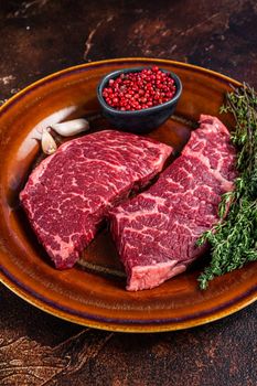 Fresh Raw denver or top blade meat steak on a rustic plate with thyme. Dark background. Top view