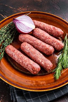 Raw kofta meat kebabs sausages on a plate with herbs. Dark background. Top view