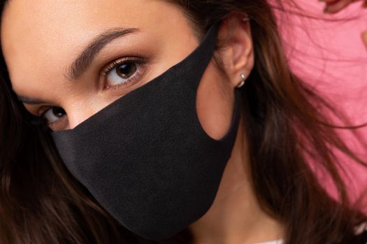 Young beautiful woman in reusable virus protective mask on face against coronavirus isolated on the pink background wall