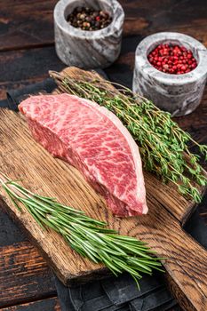 Wagyu A5 raw rump or sirloin steak, kobe beef meat on a butchery board. Dark wooden background. Top view