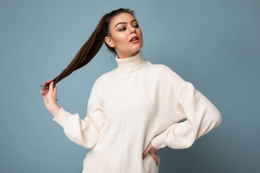 Young fascinating sexy caucasian fashion brunette woman wearing casual white sweater poising isolated on blue background wall
