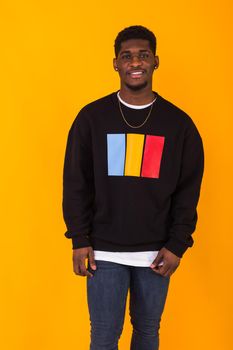 Street fashion concept - Studio shot of young handsome African man wearing sweatshirt against yellow background.