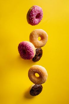 Various decorated doughnuts in motion falling on yelloy background