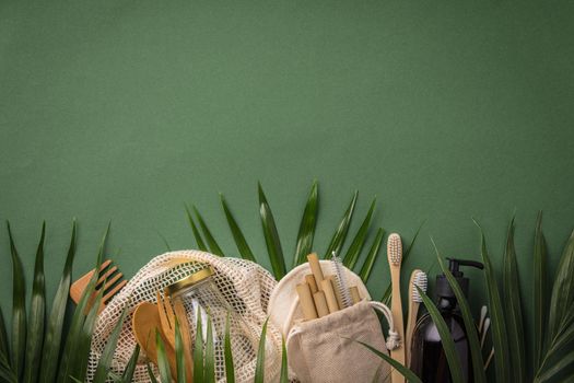 Zero waste concept. Cotton bag, bamboo cultery, glass jar, bamboo toothbrushes, hairbrush and straws on green background