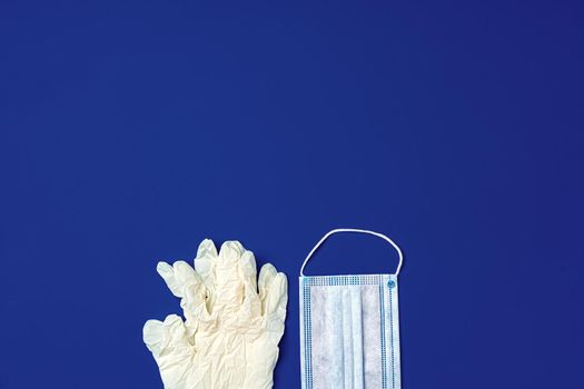 Medical gloves and surgical protective face mask on dark blue background