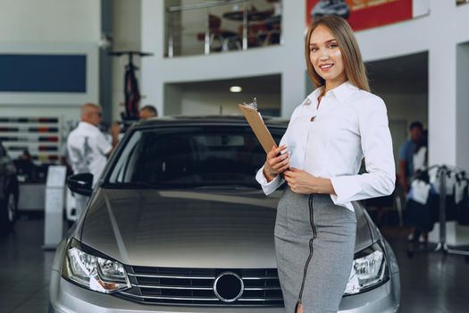 Happy beautiful young woman car dealer in showroom