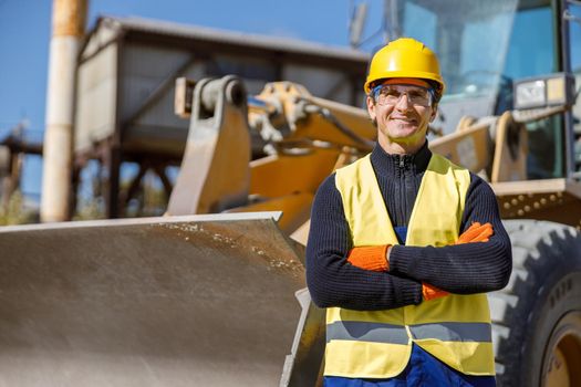 Cheerful male worker standing near tractor at factory