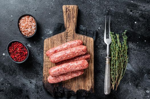 Uncooked Raw beef and lamb meat kebabs sausages on a wooden board. Black background. Top view