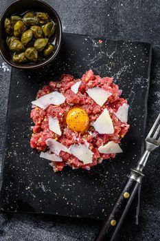 Tartar beef with a quail egg, capers and Parmesan cheese. Black background. Top view