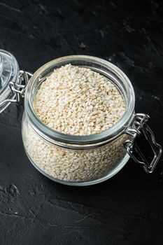 Decorticated sesame seeds, in glass jar, on black stone background