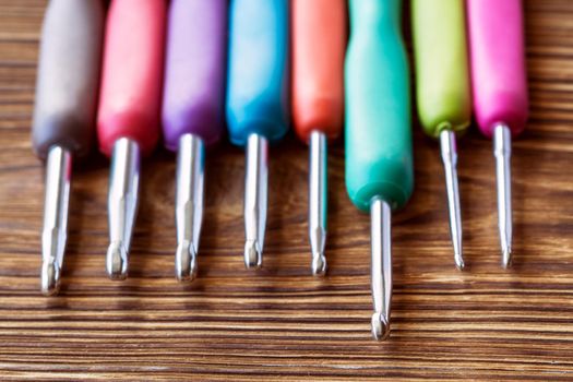 A set of multicolored crochet hooks on a wooden background. Close-up, selective focus
