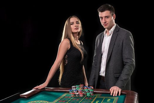 Elegant couple at the casino betting on the roulette, on a black background