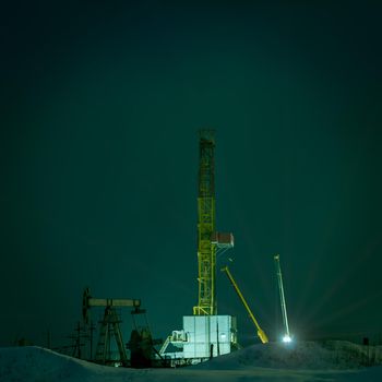 Drilling rig at night. Night view of a derrick drilling and oil pump jack.