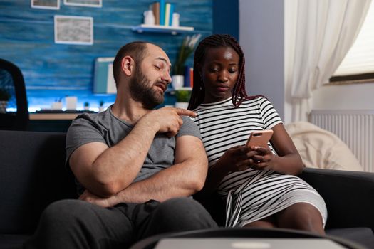 Interracial people using technology for entertainment at home. African american woman holding modern smartphone while caucasian man looking at digital gadget. Multi ethnic couple